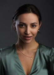 Portrait of a dark-eyed beautiful woman dressed in a green blouse, she has gold earrings and looks at camera against dark gray background, copy space