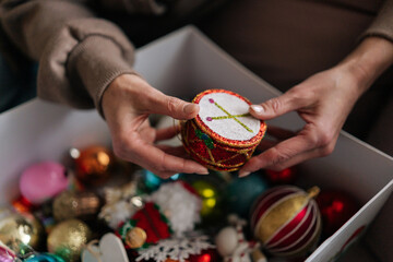 Close-up cropped shot of unrecognizable woman choosing festive toys in box for decoration Christmas tree. Preparation for holidays, decorates xmas tree for New Year. Concept of home festive atmosphere