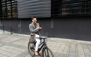 Happy employee environment lover calling colleagues before staff meeting. Cheerful businessman with glasses on reading text messages on a smart phone and pushing a bicycle.