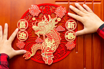 man sticking a Chinese New Year of the Dragon decoration to a door at horizontal composition translation of the Chinese words are fortune and welcome to the new year no logo no trademark - obrazy, fototapety, plakaty