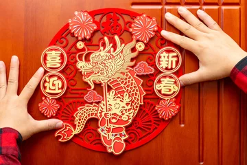 Fotobehang man sticking a Chinese New Year of the Dragon decoration to a door at horizontal composition translation of the Chinese words are fortune and welcome to the new year no logo no trademark © Freer