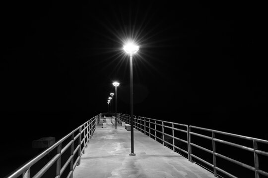 Fototapeta Black and White Long Exposure Shot of Streetlamps Glowing on Pier at Night.