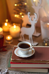Bowl of cookies, cup of tea, dry oranges, pine cones, books, reading glasses, small presents, various Christmas decorations and lit candles on the table. Cozy Christmas hygge. Selective focus.