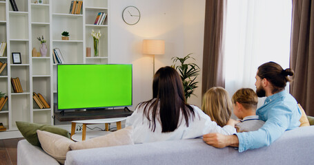 Young father and mother son and daughter sit on the couch and watch green screen TV with fun with...