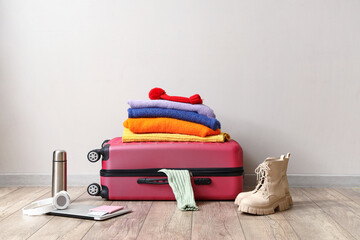 Suitcase with winter clothes and accessories near light wall