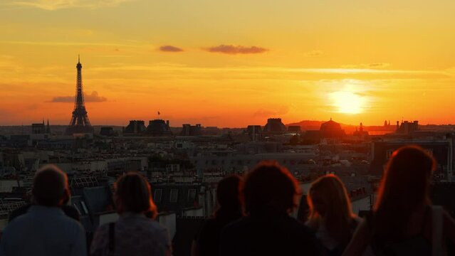 Tourists looking at the orange sunset with the Eiffel Tower in the background in Paris, France