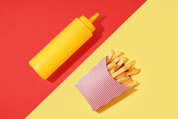 Paper box with french fries and mustard bottle on color background