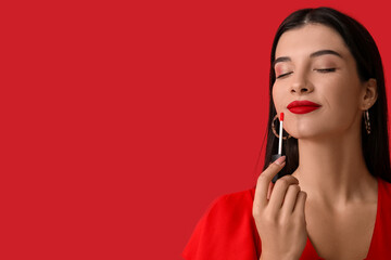 Beautiful young woman applying bright lipstick on red background