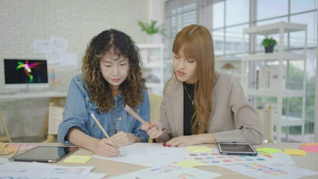 Asian colleague brainstorm, do paperwork, discuss business ideas, prepare financial report, review statistical data, engaged in teamwork
Two business young woman working together in office with report