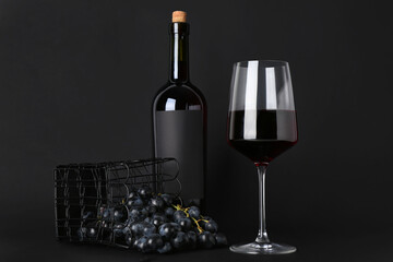 Glass and bottle of exquisite wine with grapes on black background