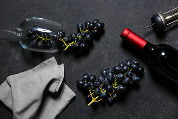 Glass and bottle of exquisite wine with grapes on black background