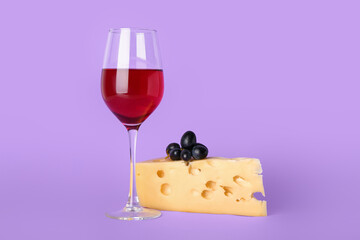 Glass of exquisite wine with cheese and grapes on lilac background