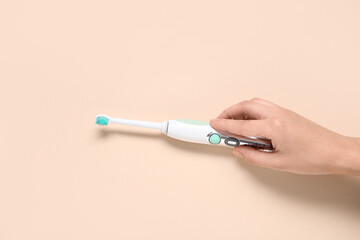 Female hand with electric toothbrush on beige background.