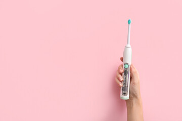 Female hand with electric toothbrush on pink background.