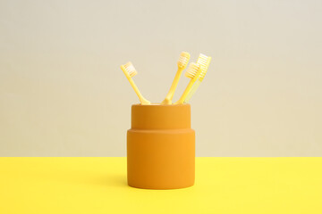 Yellow toothbrushes in orange holder on color background.