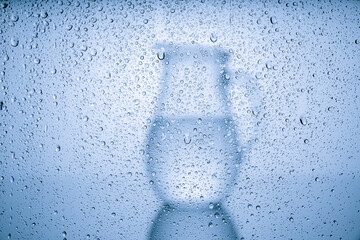 silhouette of a jug of water behind glass covered with water drops