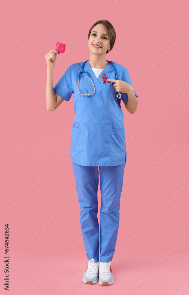 Sticker young female doctor with red ribbon pointing at condom on pink background. world aids day concept