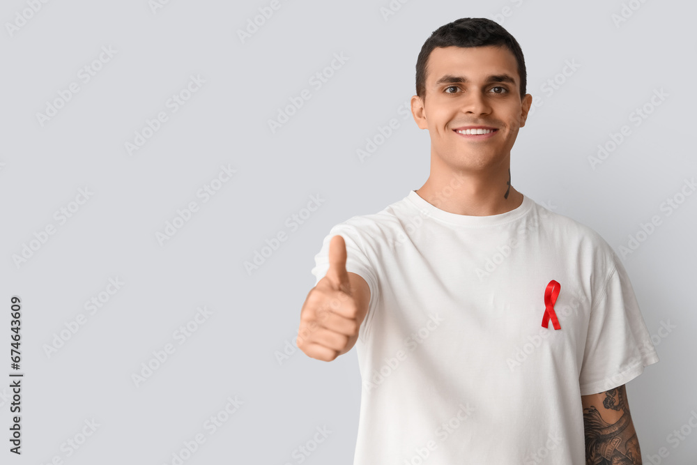 Wall mural Handsome young man with red ribbon on grey background. World AIDS day concept