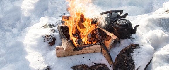 Winter campfire in the snow. Warm up with a teapot by the fire.