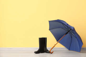 Blue stylish umbrella and gumboots on yellow background