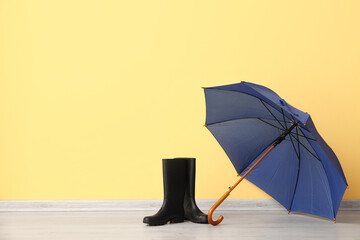 Blue stylish umbrella and gumboots on yellow background