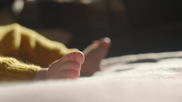 Selective focus of little tiny child lying on back in crib and moving legs. Newborn baby moves feet lying on comfortable bed at home. Toddler activity. Kid, childhood and new life concept