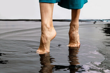 Amazing walking on water. Woman barefoot walking on the surface of the water floor. Close up legs of woman walking on floor flooded dark water - Powered by Adobe