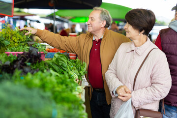 Elderly man and a woman buy greens at an open-air market