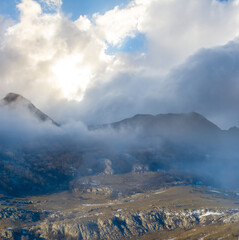 snowbound mountain valley in dense mist and clouds under a sparkle sun, winter mountain travel scene