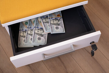 A pile of hundred dollar bills in a drawer with key lock