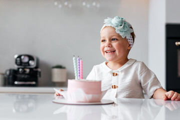 Adorable birthday girl making wish blowing candles on the cake. 3 years old toddler kid celebrating and enjoying