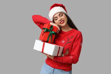 Dreaming young woman in Christmas sweater with gift boxes on grey background