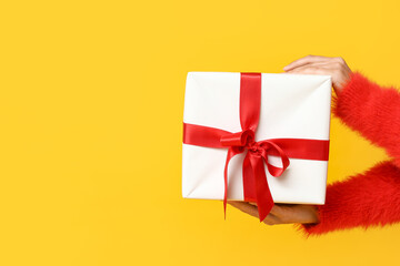 Woman with Christmas gift on yellow background