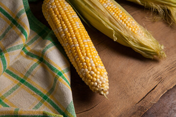 Close up view of three cobs sweet corn with green leaves on wooden background..