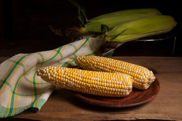 Clay plate with two cobs sweet corn on wooden background..