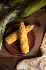 Clay plate with two cobs sweet corn on wooden background..