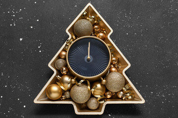 Plate in shape of Christmas tree with alarm clock and balls on black background