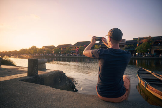 Man photographing Hoi An cityscape. Tourist with smart phone in ancient city during golden sunset, Vietnam...