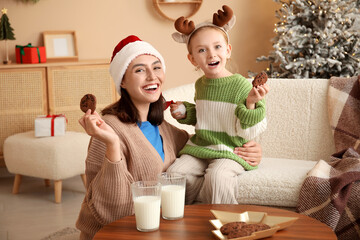 Fototapeta na wymiar Happy mother and her little daughter eating cookies with milk at home on Christmas eve