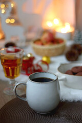Obraz na płótnie Canvas Cup of tea or coffee, glass of wine or juice, bowl of cookies, organic pomegranate, fluffy blanket, pine cones, various Christmas decorations and lit candles on the table. Christmas hygge concept.