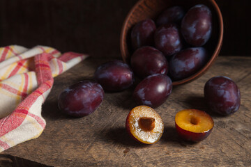 Whole and half of purple plums on wooden background. .