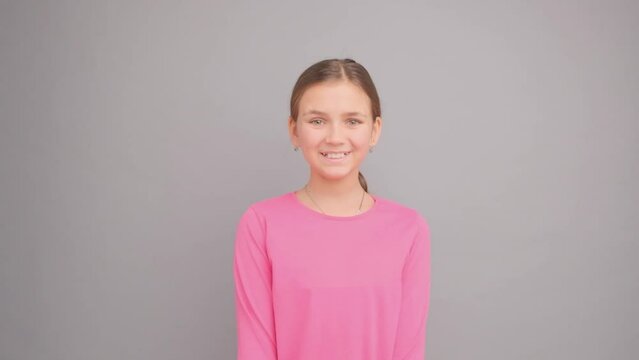 Portrait of a smiling girl on a gray background with a pink T-shirt.