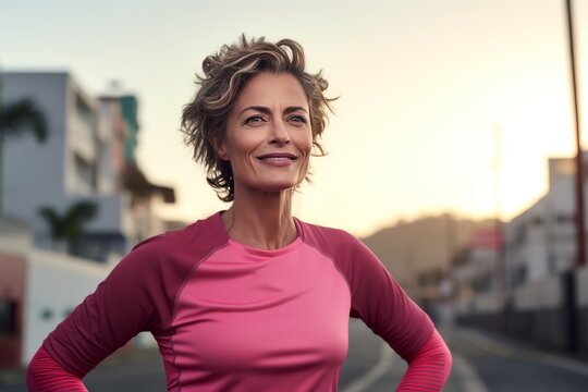 Close-up portrait of slender mature Caucasian woman in sportswear while training outdoor. Attractive smiling lady jogging or working out in city street. Active lifestyle in urban environment.