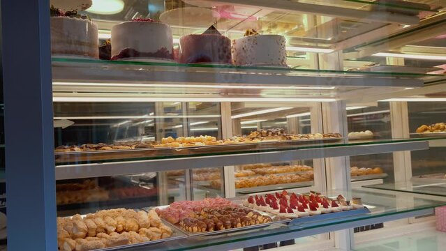 Glass Pastry Shop Display Case With Choice Of Cream Cake Or Fruit Cake Variety Of Cake With Frosting In Bakery Refrigerator. Sweet pastries with berries. Confectionery Showcase.