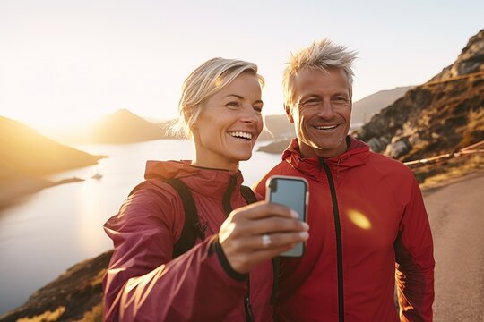 Adult sporty couple making pause while jogging, walking or workout in picturesque seashore. Mature Caucasian man and woman in sports outfit making selfie and smiling. Active lifestyle.