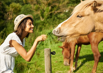 Woman, horse and outdoor for feeding grass with smile, care or love for pet at farm, countryside or...