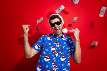 Photo of young winner christmas lottery successful businessman wear blue shirt santa print flying dollars isolated on red color background