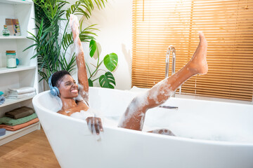 Attractive black woman wearing headphones with music in foam bathtub. Beauty, skin care, home spa and wellbeing concept. High quality photo