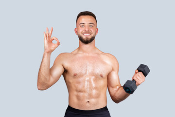 Smiling sweat confident muscular young european man with beard, naked torso make exercises with dumbbell, show ok