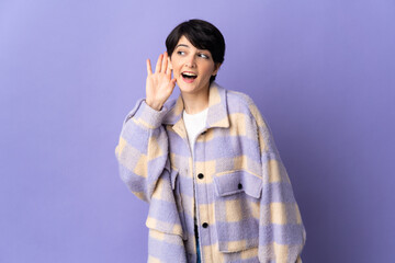 Woman with short hair isolated on purple background listening to something by putting hand on the ear